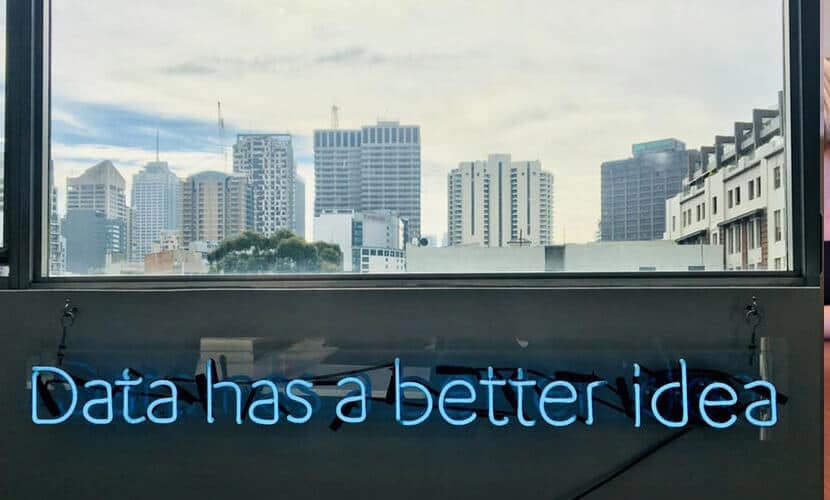 A neon sign that reads "data has a better idea" is in front of a background of large buildings.