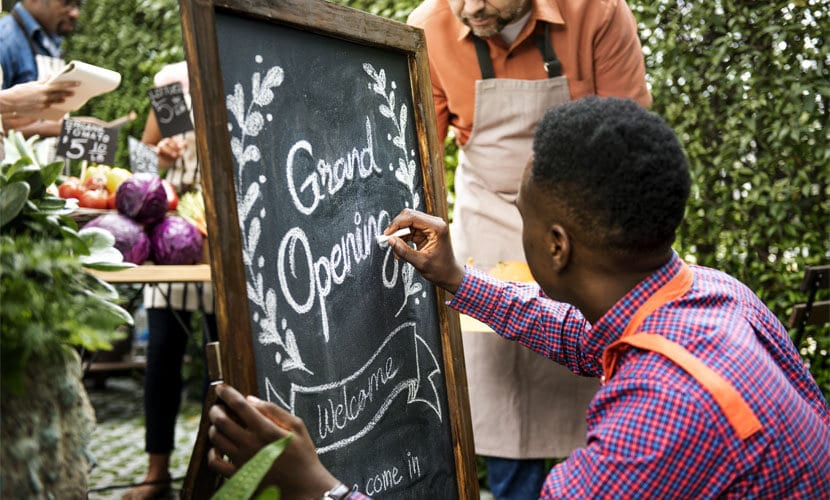 A man writing Grand Opening on a chalkboard outside of the retail space